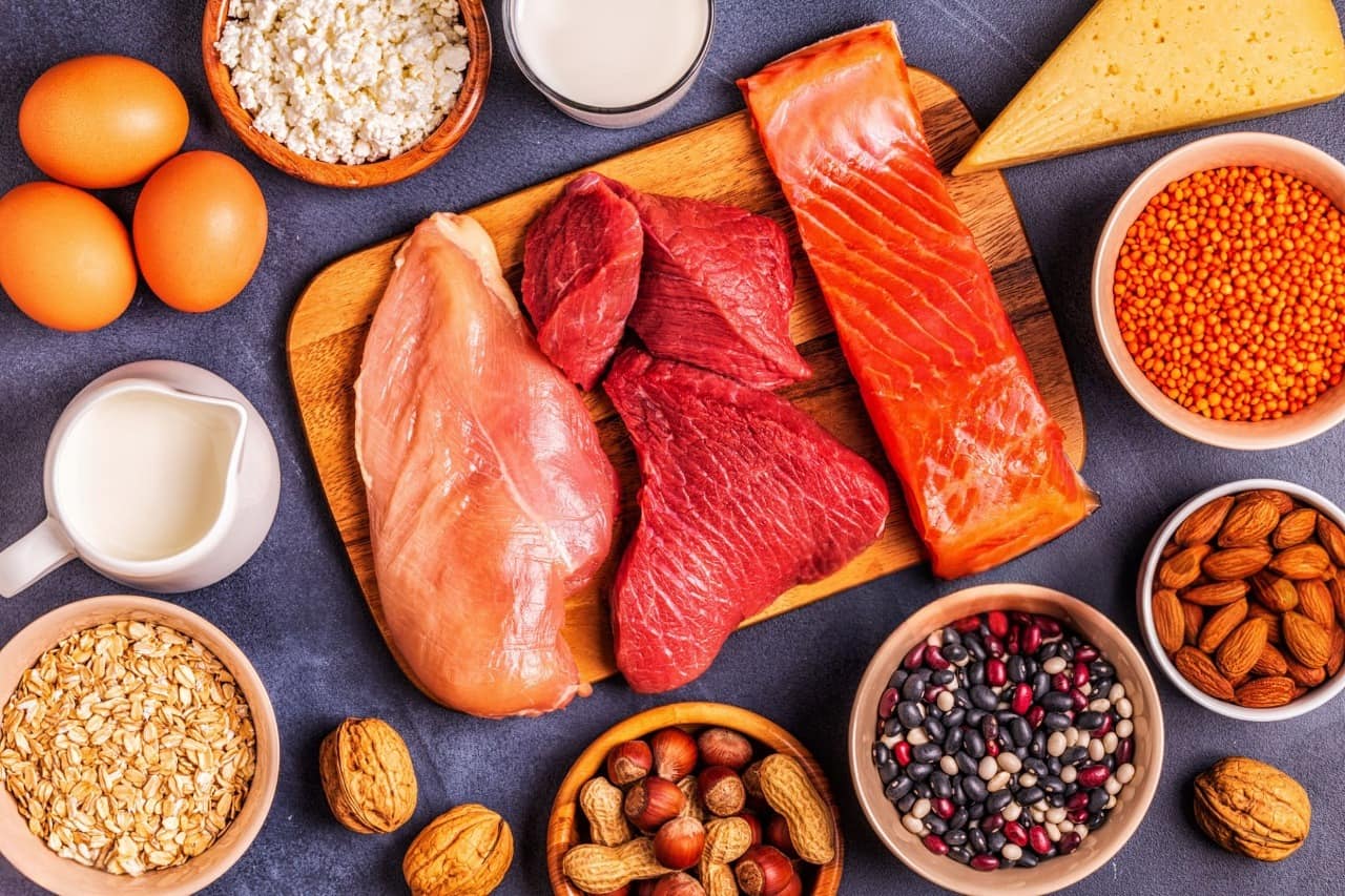 Разнообразные источники белка: мясо, рыба, яйца, молочные продукты, орехи и бобовые на деревянной доске