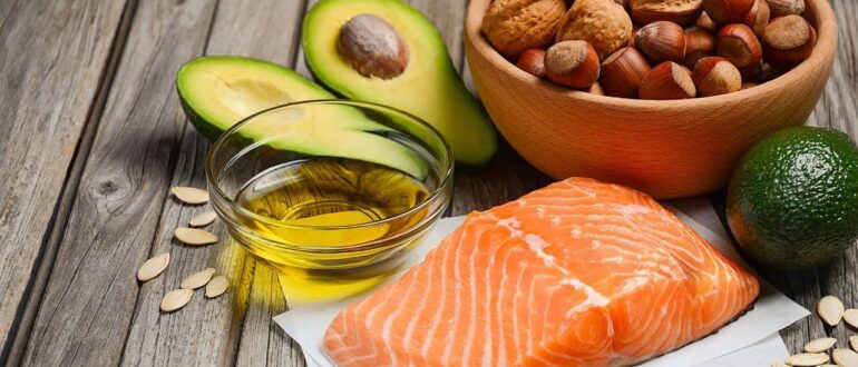 Продукты с полезными жирами: кусок лосося, авокадо, орехи, семечки и растительное масло на деревянном столе